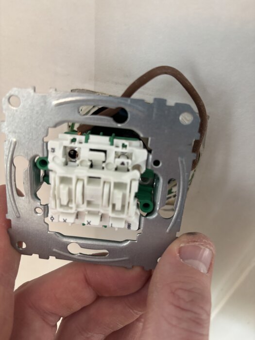 Elektrisk strömbrytare med exponerade kablar monteras i en vägg. En hand håller brytaren på plats.