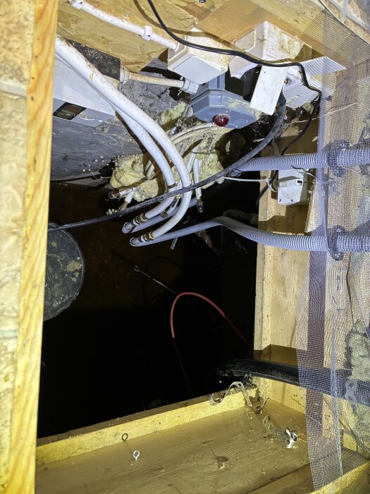 Rör och elektrisk installation i utrymme med vattenpump, omgivet av träkonstruktion och isoleringsmaterial.