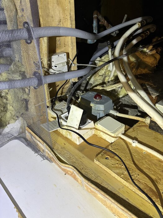 Rör och kablar i ett köksutrymme med träpanel och gips, relaterat till grundvattenpumpning och frusna rörmynningar.