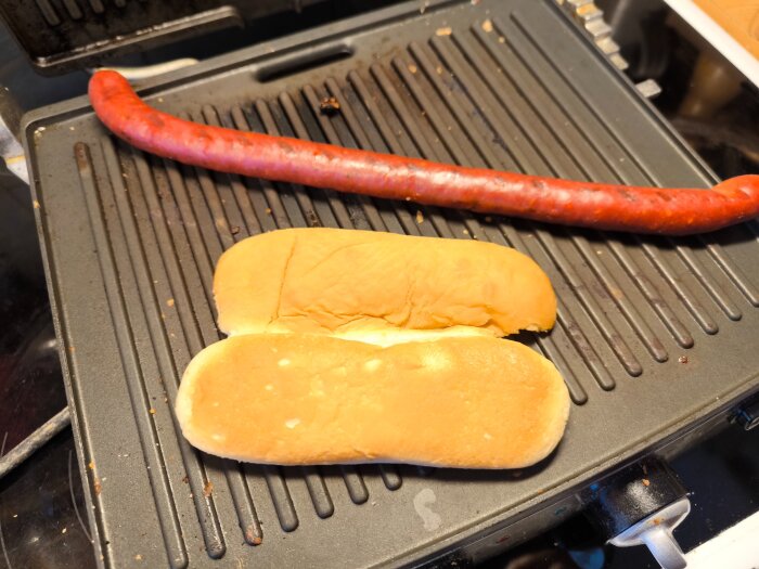 Korv och korvbröd på en grillpanna. Korven är längre än bröden.