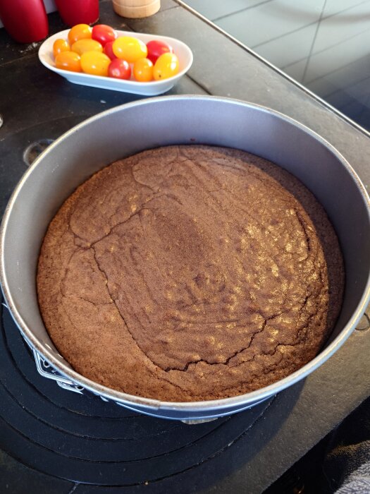 Chokladkaka i springform på köksbord, bredvid en skål med färgglada tomater.