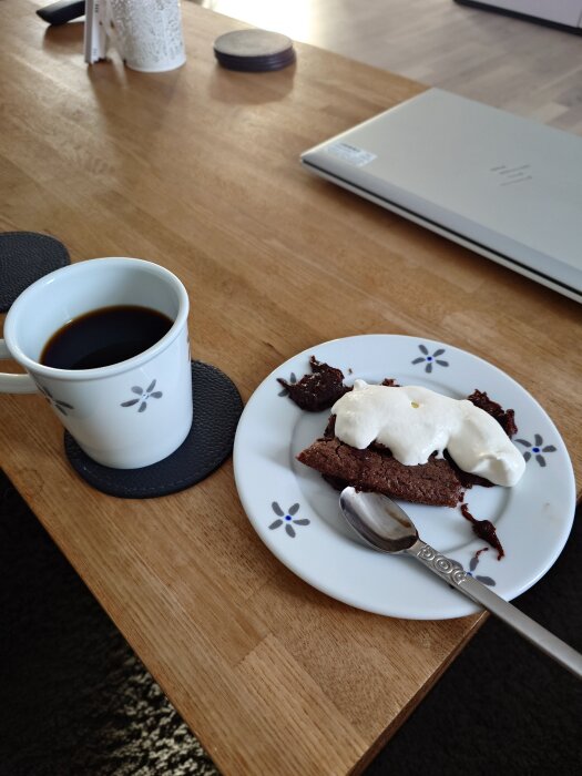 Kopp kaffe och tallrik med kladdkaka toppad med grädde på ett träbord.