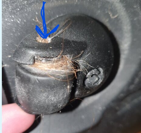 En närbild av en skruvplats utan skruv, omgiven av damm och smuts, med en finger pekande mot hålet, markerad med en blå pil.