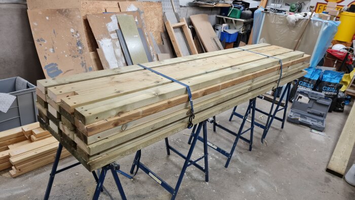 Staplade tryckimpregnerade träreglar på bockar i ett garage, klara för byggprojekt.