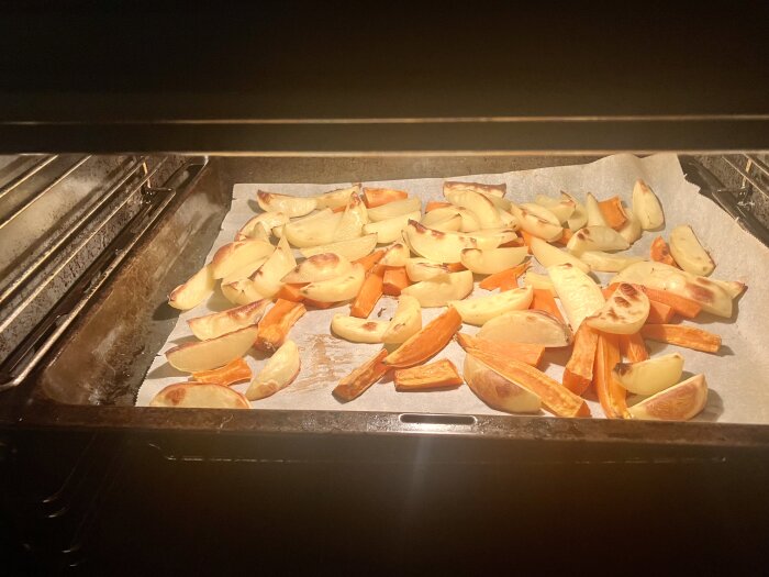 Klyftpotatis och sötpotatis på en bakplåtspapper i ugnen.