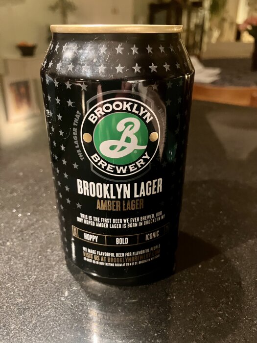En burk Brooklyn Lager Amber Lager med svart design och stjärndetaljer står på en bordsyta.