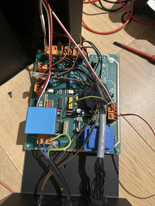 Elektroniskt kretskort med flera färgade ledningar och komponenter för en Ecotec panna, ligger på ett trägolv.