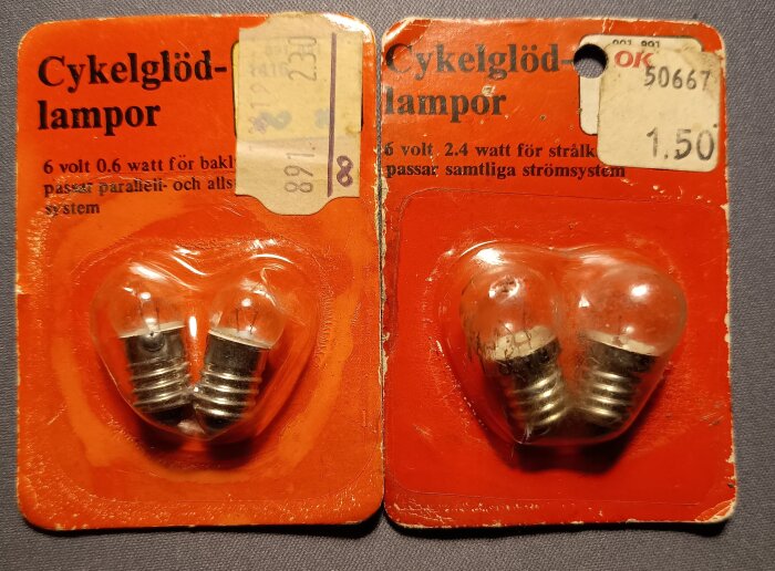 Två förpackningar med cykelglödlampor, båda med orange bakgrund. En för baklyktor, 6V 0.6W, och en för strålkastare, 6V 2.4W.