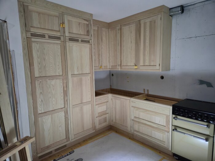 Kök under renovering med träluckor och en gul spis, väggar saknar ytskikt.
