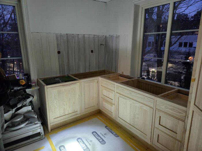 Köksrenovering pågår med nyinstallerade träluckor och förberett tak för taklister vid fönster, inomhus kvällstid.