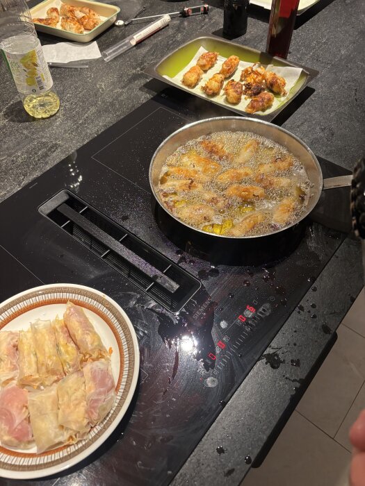 Stekning av vietnamesiska vårrullar på spishäll med två fat vårrullar bredvid.