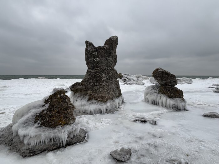 Isiga raukar vid en kustlinje med havet i bakgrunden under en mulen himmel.