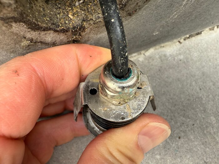 Närbild på en hand som håller en rund, silverfärgad lampa med en svart kabel, monterad i en betongyta.