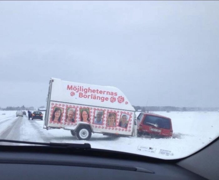 En röd bil och släpvagn med texten "Möjligheternas Borlänge" har kört av en snöig väg. Människor på bilder visas på släpvagnen.