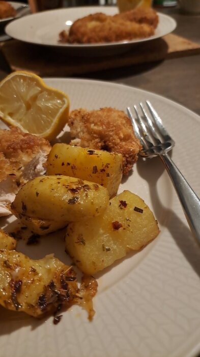 Kycklingschnitzel serverad med råstekt dragonpotatis och en citronklyfta på en tallrik.