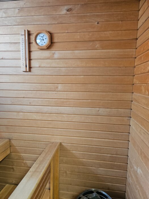 Vägg av träpanel i en bastu med en termometer och en hygrotermometer.