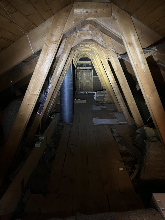 Vind med trägolv, takbjälkar och ett ventilationsrör, sedd i skenet av en ficklampa.