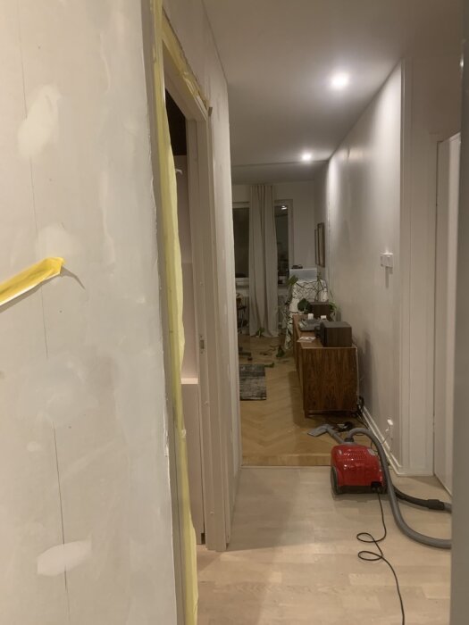 Vitlaserat golv i en hall med maskin för slipning av golv synlig; arbetet syftar till att ändra golvets nyans till gulbrunt, likt fiskbensparkett.