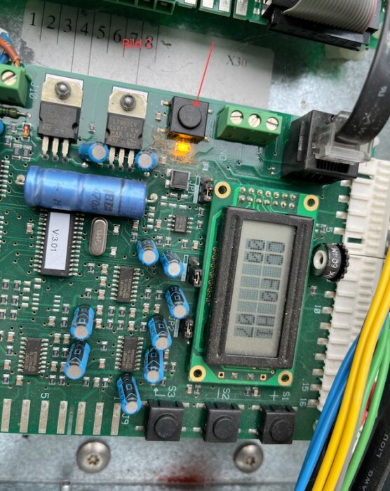 Reset-knapp som blinkar bredvid en belyst säkring på elektronikkortet i ett värmesystem, med anslutna kablar och en liten skärm.