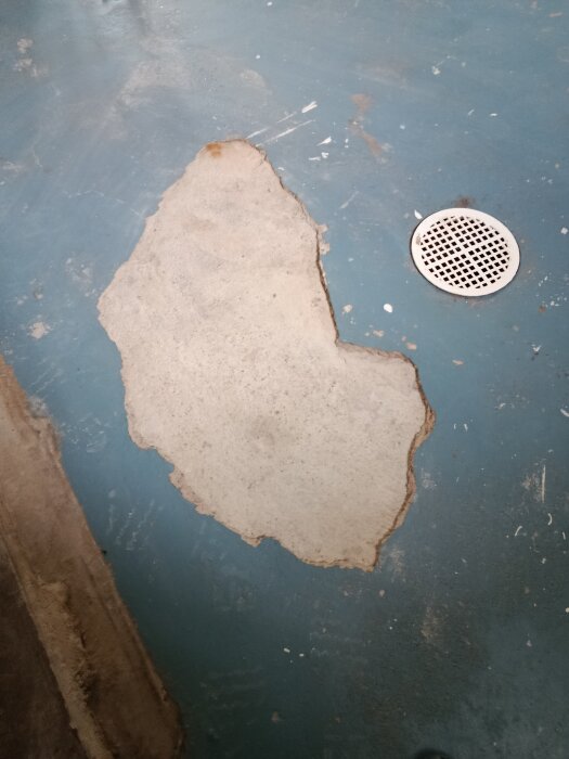 Skadat golv med bortknackat översta lager och avlopp, cirka 1-2,5 cm djup, i ett gammalt tvättrum, förberett för fyllnadsmaterial.
