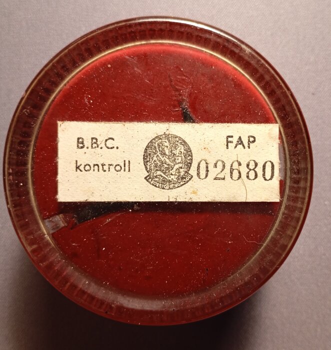 Rund burk med röd lock och etikett med texten "B.B.C. kontroll" och nummer "02680", samt en logotyp i mitten.