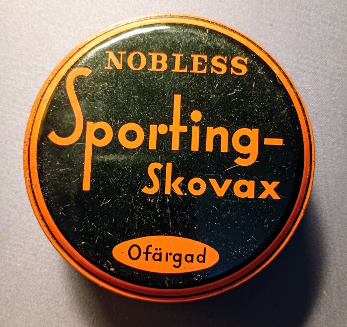Rund burk med texten "Nobless Sporting-Skovax Ofärgad" i orange på svart bakgrund.