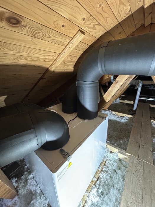 Ventilationssystem i en vindsvåning med isolerade rör och trälister i taket.