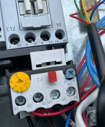 Elektrisk kopplingsbox med ledningar och terminaler, inklusive en testknapp och skruvanslutningar. Flera färgade kablar anslutna.