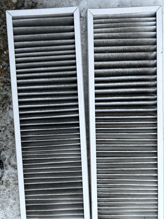 Två nya, bytta metalliska ventilationsfilter ligger på marken.