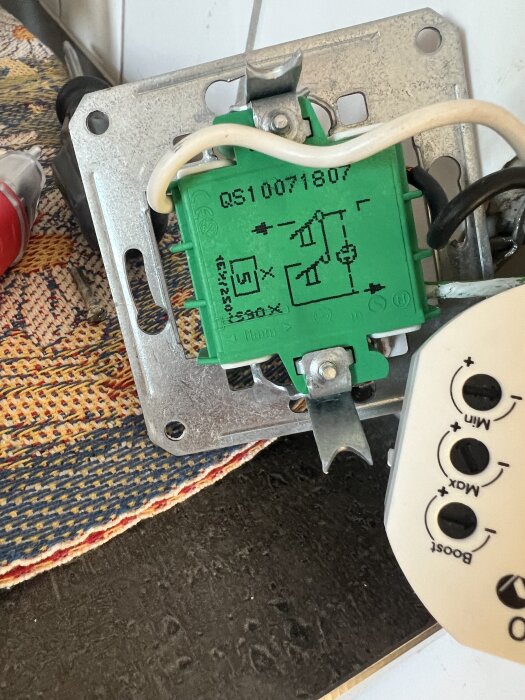 Elektrisk installation med en grön modul och vit sladd, monterad på en metallplatta. Funktionen verkar relatera till en dimmer.