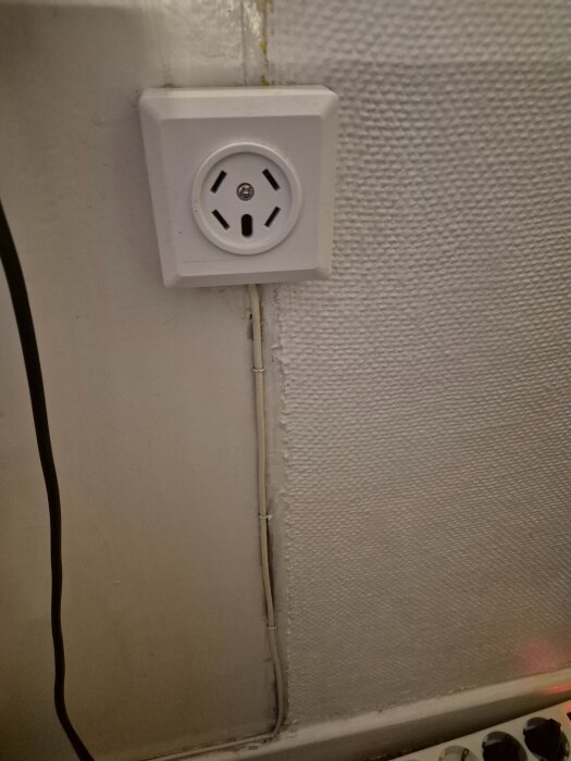 Vitt telejack på väggen med kabel som löper neråt, bredvid det texturerade väggmaterialet.