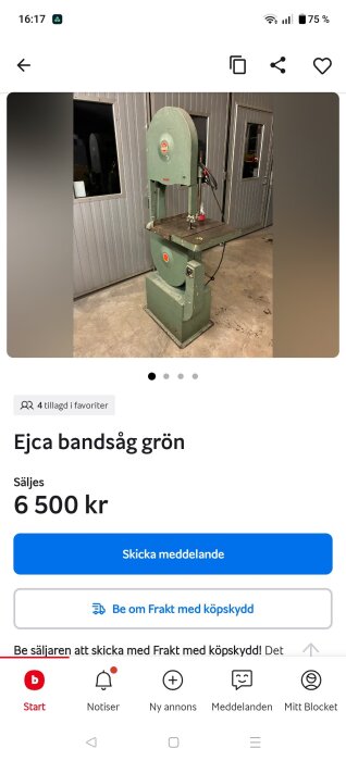 Grön bandsåg av märket Ejca står på ett betonggolv nära en grå plåtvägg med fönster och dörrar i bakgrunden.