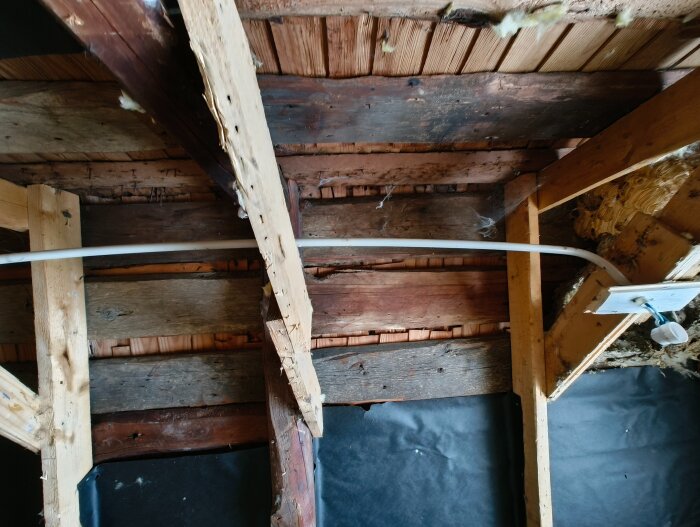 Träram och bjälkar i äldre hus, synliga på en övervåning. Renoveringsprojekt pågår, med fokus på takisolering och luftspalt. Inga fukttecken.