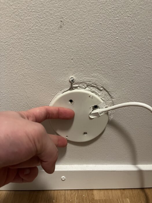Hand pekar på ett vägguttag med trasigt doslock och nätverkskabel, visar oregelbunden passform för nytt RJ45-uttag.