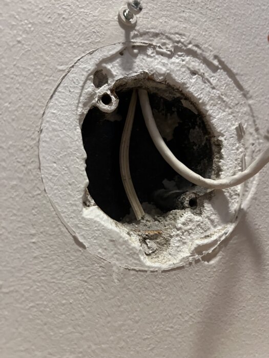 Öppet vägguttag från 50-talet med blottade kablar och en ojämn yta, redo för installation av ett RJ45-uttag.