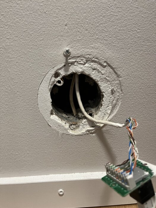 Väggöppning med sladdar och exponerade kablar, äldre elinstallation utan korrekt nätverksuttag, trasigt doslock och ojämna fästpunkter.