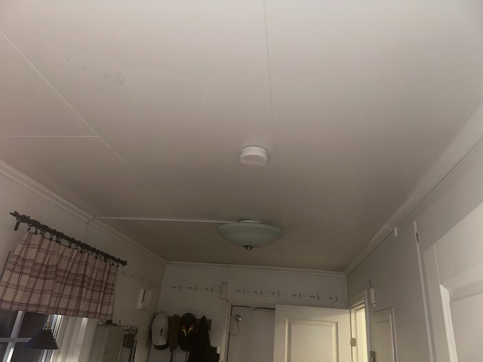 Vit tak med lampor och hängande gardin. Taket ska få tre nya dimbara LED-spotlights inbyggda på rad från ytterdörren till fotopositionen.