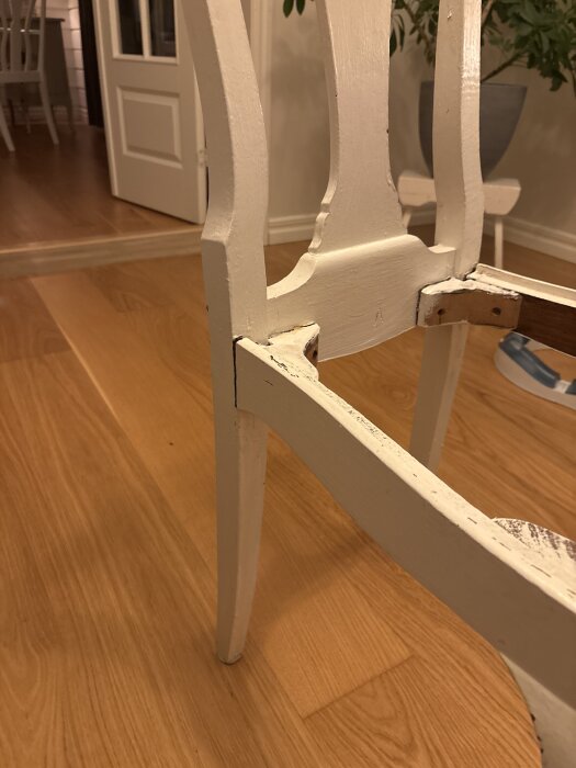 Trasig trästruktur vid bakdelen av en köksstol, visar skador och behov av reparation.