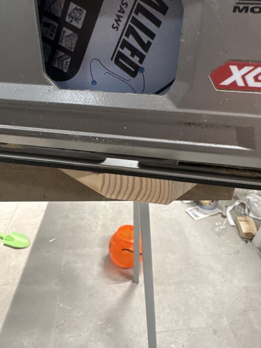 Sågklinga monterad felriktat på såg med orange plastkorg och grönt spade på golvet i bakgrunden.