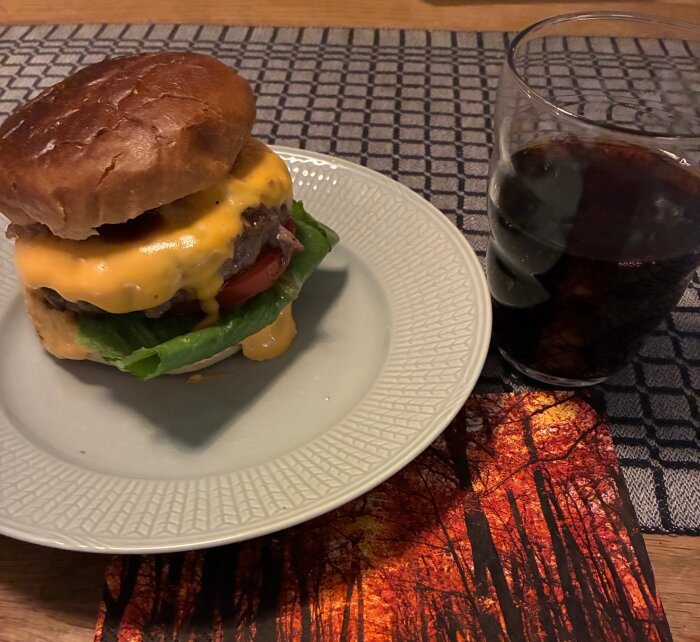 Burger med cheddarost, sallad och tomat på en tallrik bredvid ett glas med julmust.