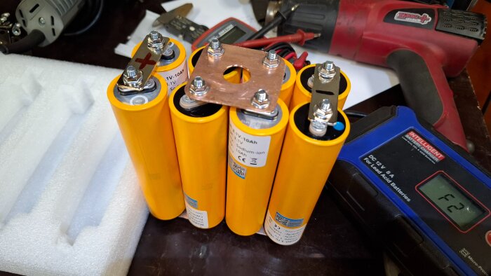 Gula litiumjonbatterier grupperade, omgivna av verktyg och en batteriladdare på en arbetsbänk.