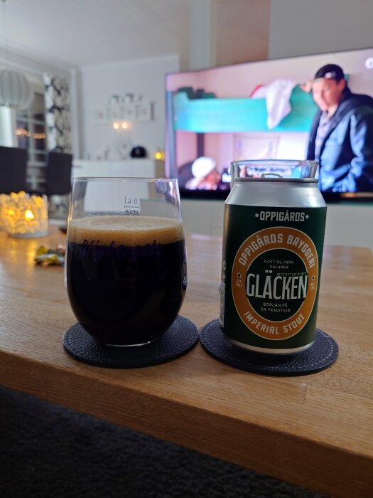 Ett glas med mörk öl bredvid en ölburk med etiketten "Glacken Imperial Stout" på ett bord, med en TV i bakgrunden.