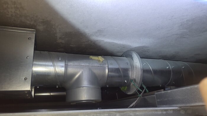 Ventilationsrör sett från inspektionslucka i hallen med tejp och buntband fäst över ett skarvställe.
