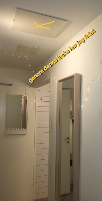 Kryssmarkerad lucka i taket ovanför dörr med spegel och väggprydnader i form av ljusslingor.