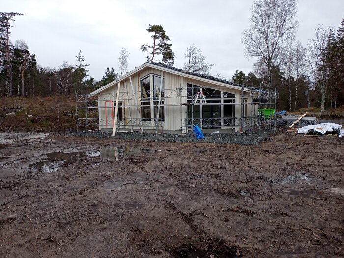 Ett halvfärdigt hus i byggfas med ställningar runtom och en rödmarkerad plats som indikerar öppning för en ny altandörr.