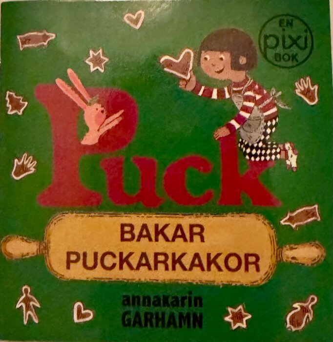 Omslaget till boken "Puck bakar puckarkakor" med illustration av ett barn i randig tröja och ett rullande bakverk.