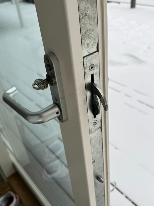 Dörr med metalldörrhandtag och lås, nyckel insatt, ståendes ovanpå snötäckt altan.