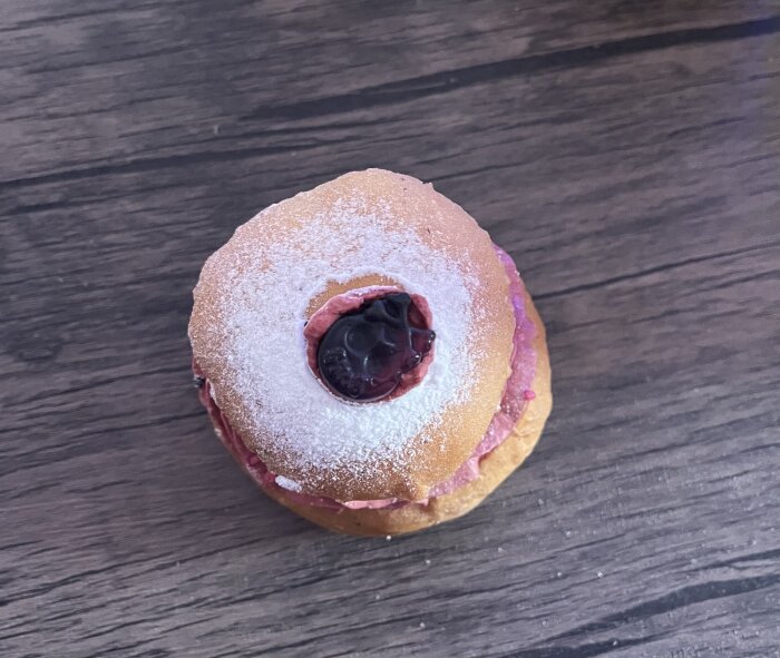 Bulldeg med florsocker och rosa fyllning toppad med bär på träbord.