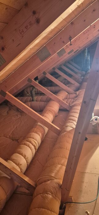 Vindsutrymme med isolerade ventilationskanaler, drev och synliga takbjälkar.