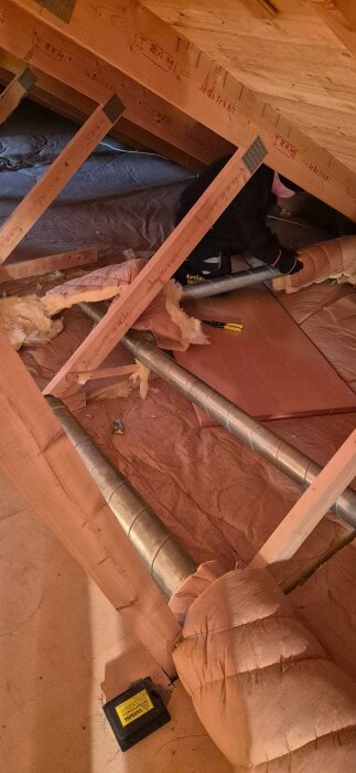 Person som river ventilationskanaler och isolering under bygge, fokuserat på en träsektion med synliga rör.